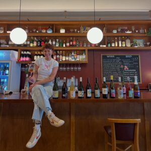 Louise Marks, owner of Bar Lou Lou, sitting on the bar with a glass of wine