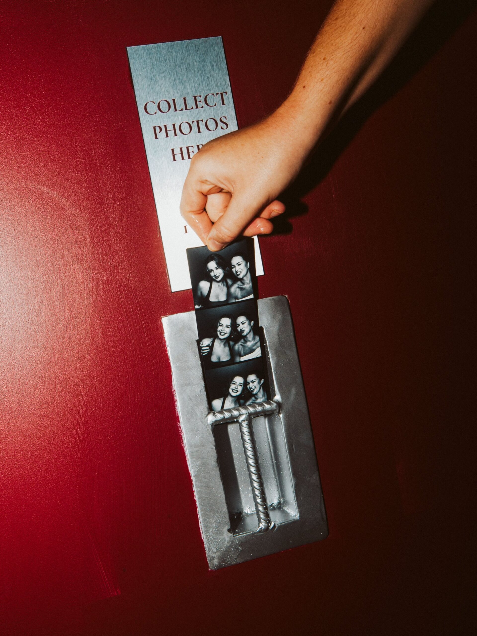 Hand holding a black-and-white photo strip at the Juliet's Photobooth collection slot