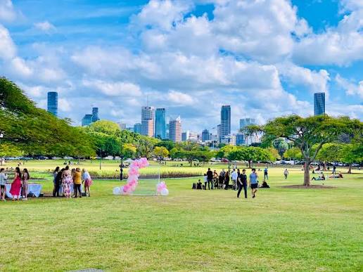 Park lawn with a pink balloon arch and Brisbane city skyline behind, illustrating New Farm named among the world’s coolest neighbourhoods
